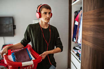 Teen holding a laundry basket and wearing headphones