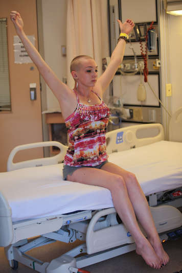 girl sitting on edge of hospital bed with arms raised in ego eradicator pose