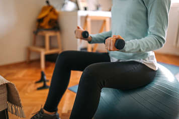 Teen sitting on ball holding hand weights