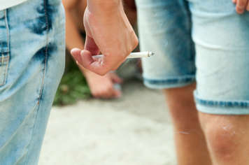 Closeup on a teen's hand holding a lit cigarette