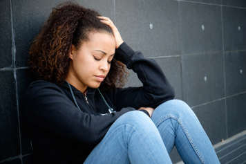 Teen sitting on a floor up against a wall with their eyes closed and holding their head up with their hand