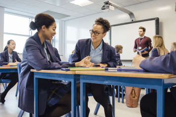 Students in uniforms of button-down shirts, blazers and skirts or dress pants sitting at desks in a classroom