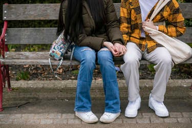 Two teens sitting beside each other on a park bench and holding hands