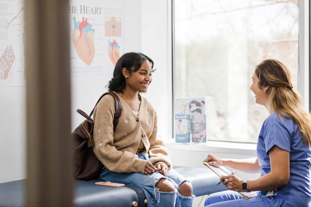 Teen girl sitting on an exam table talking to a health-care provider