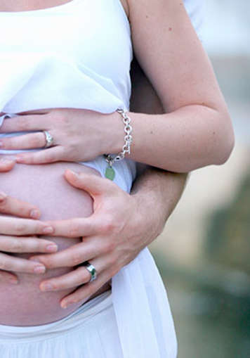 Pregnant woman and partner placing hands on her belly