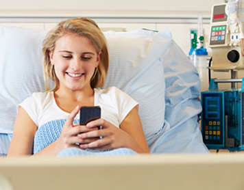 Teen girl using a phone while in hospital bed