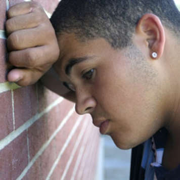 Teen boy resting head against a wall and looking sad