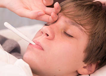 Boy lying in bed with thermometer in mouth